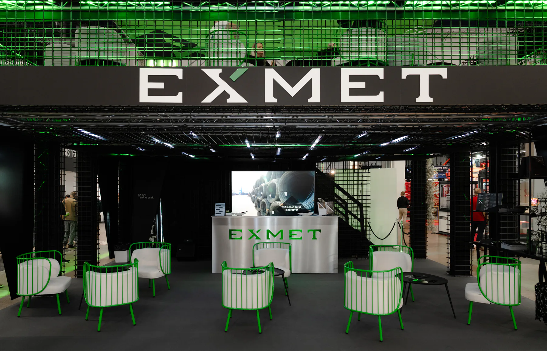 Front of the Exmet stand at FinnBuild with green chairs under the EXMET sign